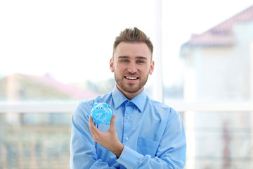 Canvas Print - Happy young man holding piggy bank on blurred background