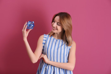 Sticker - Happy young woman holding piggy bank on color background