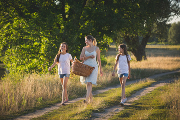 Portrait of happy mother with two daughter walking by the river in meadow