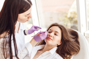 Wall Mural - Correction and eyebrow styling in salon. Beautiful woman gets eyebrow correction procedure. Female customer is lying on a white couch.