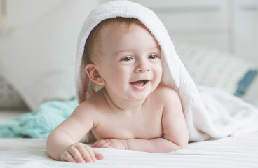 adorable smiling baby in hooded towel lying on bed after having bathtime