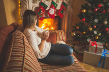 Woman Relaxing By The Fireplace And Christmas Tree With Cup Of Tea