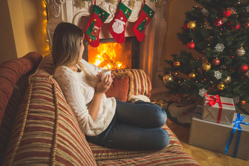 Woman relaxing by the fireplace and Christmas tree with cup of tea