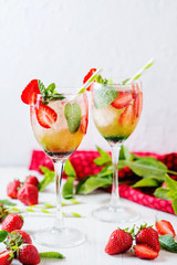 Wall Mural - Alcoholic and non-alcoholic refreshing drinks, cold sparkling cocktail with ice, green mint and fresh strawberries in a beautiful glass on a light background 