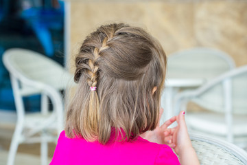 Wall Mural - Braided hair for a girl 4-5 years. Back view. A child in a pink blouse is sitting in a beauty salon.