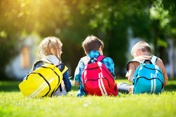 Wall Mural - Children with rucksacks standing in the park near school. Pupils with books and backpacks outdoors