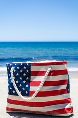 Bag with American flag colors near ocean on the sandy beach