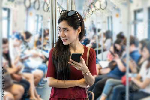 Zdjęcie XXL Azjatycki kobieta pasażer z przypadkowym kostiumem używać ogólnospołeczną sieć przez mądrze telefonu komórkowego w BTS Skytrain poręczach lub MRT metrze dla podróży w dużym miasta, stylu życia i transportu pojęciu,