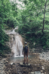 Wall Mural - Hiker Has Reached The Destination And Enjoying View Of Waterfall And Beauty Unspoilt Nature. Contemplation Adventure Concept