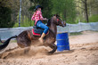 A barrel racer at a rodeo makes an explosive turn around one of the barrels, sending arena sand flying in all directions