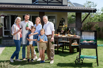 Wall Mural - Happy family of three generations standing together on green lawn and smiling at camera