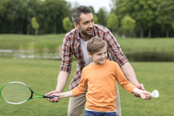 portrait of father teaching little son playing badminton outdoors