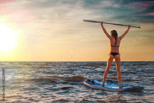 Zdjęcie XXL Kobiety ćwiczy SUP joga przy zmierzchem, medytuje na paddle desce.
