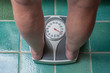 A severely overweight person weighing herself or himself on a bathroom scale