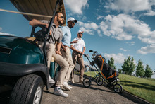 Group Of Smiling Friends Standing Near Golf Cart And Looking Away