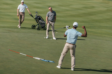 Wall Mural - african american golfer celebrating success with his friends on green pitch