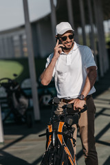 Wall Mural - smiling golf player talking on smartphone before golf game