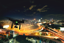  Drone (Multi-rotor) Silhouette Flying Above The City Panorama At Night Scene.