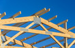 A new build roof with a wooden truss framework with a blue sky background.