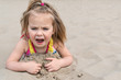 Little girl lying on the sand on the beach screaming mouth wide open, close-up