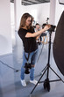 © Photodrive - Young female photographer work in studio. Beautiful woman with camera is setting photographing equipment in studio getting ready for a photo shoot