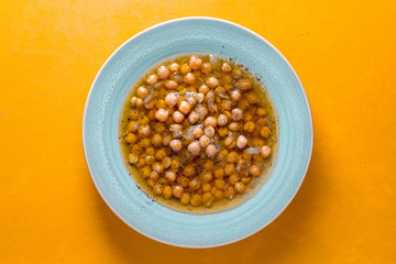 Greek chickpea soup in the white plate on the yellow background  top view