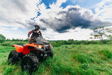 Man On The ATV Quad Bike In A Field. Blue Sky With Clouds.