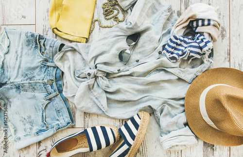 Plakat Letni strój płaski. Pastelowe lato kobiet ubrania, parkietowy tło, odgórny widok. Niebieskie spodenki jeansowe, lniana koszula, słomkowy kapelusz, żółta torebka, okulary przeciwsłoneczne, niebiesko-białe paski z apaszką, espadrillas