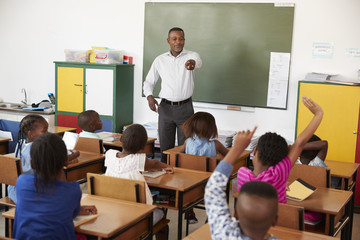 Wall Mural - Teacher and kids with hands up in an elementary school class