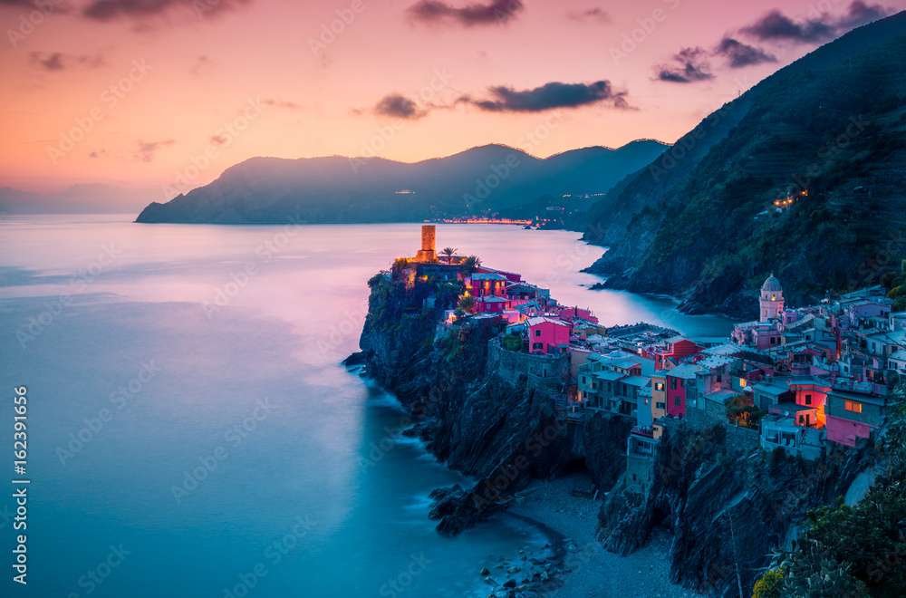 view of famous travel landmark destination Vernazza,small mediterranean old sea town with harbour coast and castle,Cinque terre National Park,Liguria, Italy. Summer colorful sunset with street lights - obrazy, fototapety, plakaty 