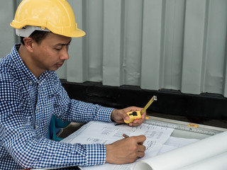 Wall Mural - Engineer or Architect sitting working at his desk in the office checking on blueprint.