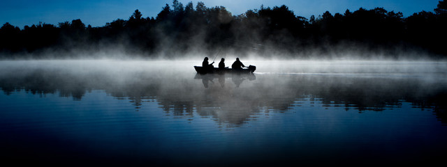 silhouette of fisherman on misty blue lake