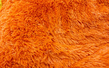Fluffy Texture Fabric. Closeup Of The Pillow With Orange Fur Cover. Abstract Background.