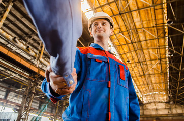 Handshake of two men of engineers in white helmets and protective overalls against the background of a metallurgical plant. Completion of the transaction. conclusion of a contract. 