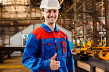 A man is showing his thumb up. An employee in overalls and a white helmet of an industrial plant shows a class. Gestures.