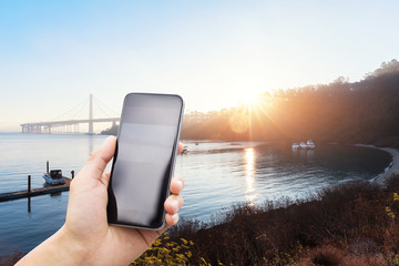 Wall Mural - mobile phone with suspension bridge at sunrise