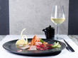 Mixed sashimi on a black plate with a glass of white wine and soy sauce