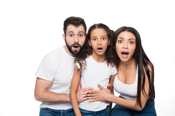 Surprised multiethnic family sitting together and looking at camera isolated on white