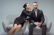 businesswoman whispering something on colleague's ear while sitting on chairs