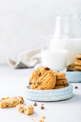 Wall Mural - Stack of chocolate chip cookies on blue stone plate with glass of milk on light gray background. Selective focus. Copy space.