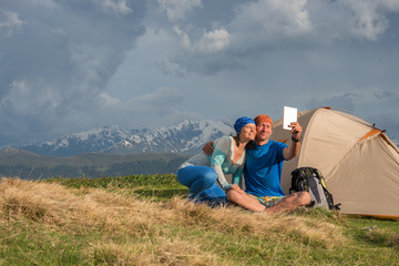 Funny travelers sit next to tent, use table, taking selfie