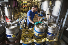Man Working In A Brewery, Stacking Metal Beer Kegs.