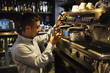 © Mint Images - Side view of man standing at an espresso machine, frothing milk.