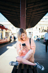 Young woman sitting at the train station and using mobile phone  