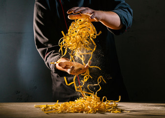 Chef adds wheat flour to the Italian ribbon-shaped pasta, before preparing the dish. Freeze motion effect. Strong contrast side lighting.