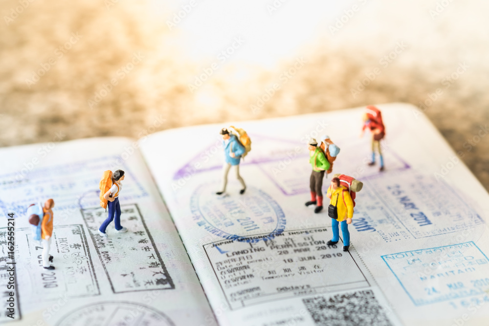 Travel Concept. Group of miniature with backpack walking and standing on passport with immigration stamps. - obrazy, fototapety, plakaty 