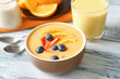 Bowl of fresh yogurt smoothie with orange and berries on wooden background