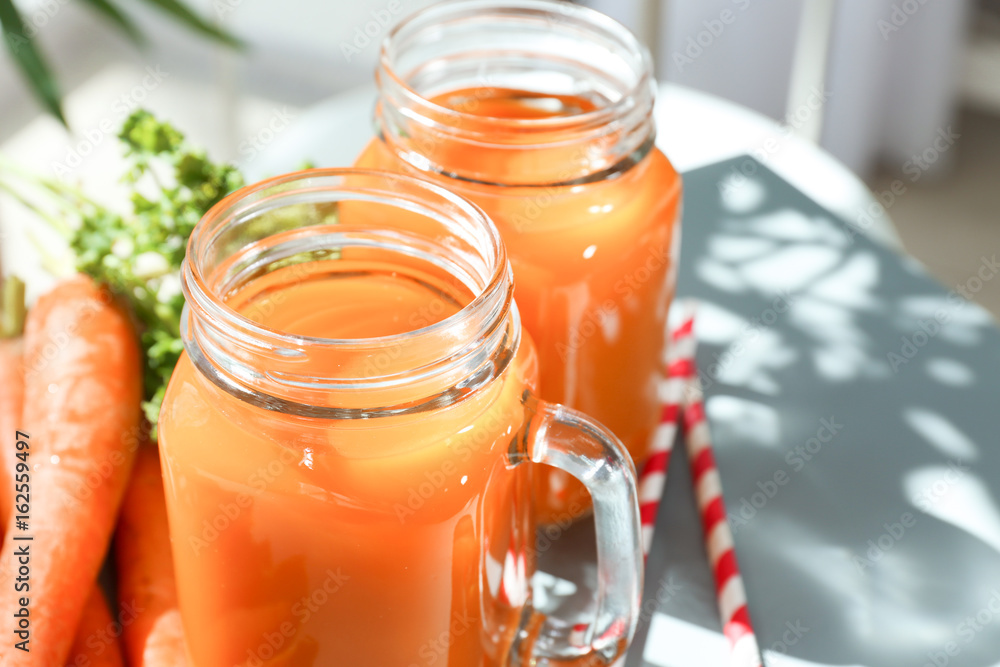 Mason jars of fresh carrot juice on table, closeup