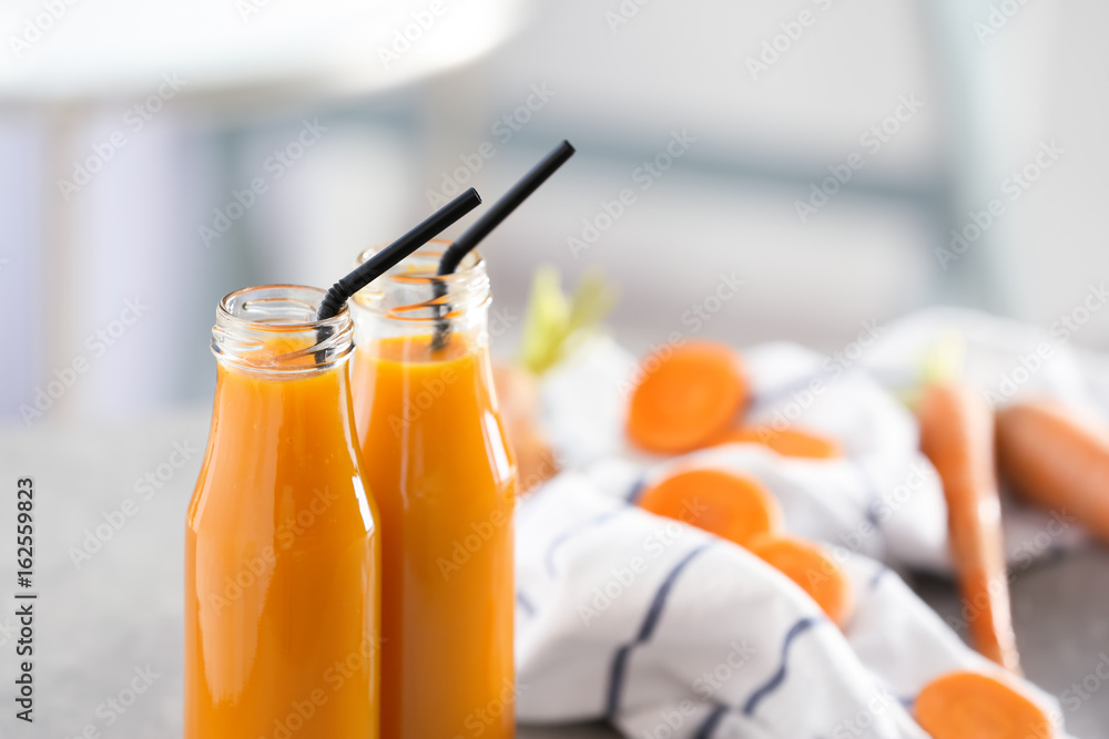 Bottles of fresh carrot juice on blurred background