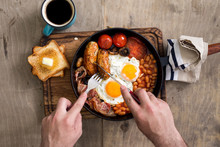 Man is eating English breakfast on wooden light table